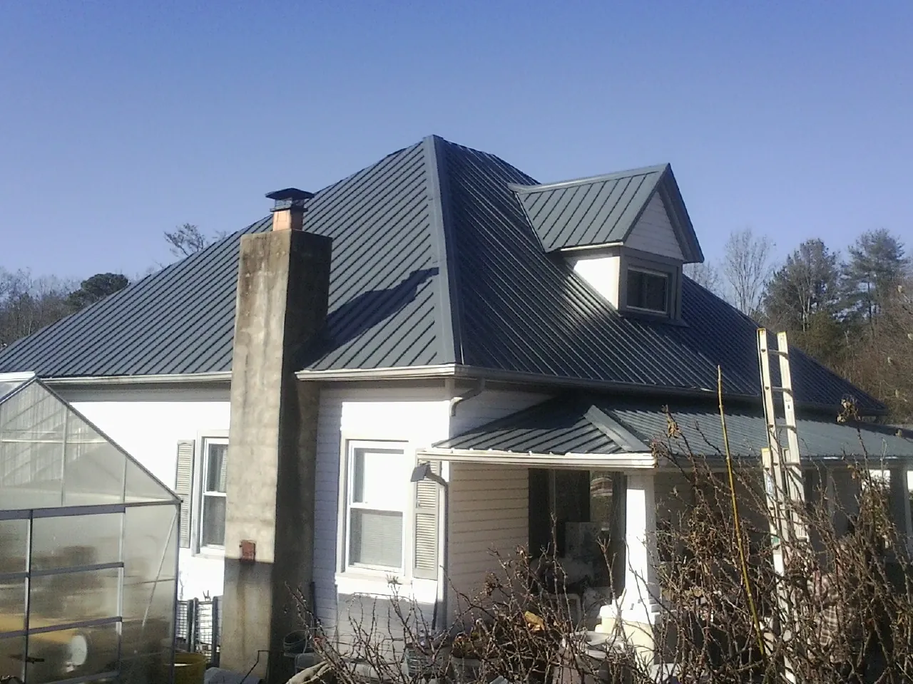 Dark blue standing seam metal roof on a white farmhouse with dormer — Slate & Tile Roof Repair by Roofing Brothers in Brownell