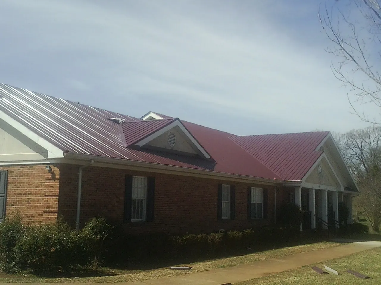 Red metal roof with gabled entries on a long brick building, from a Hail Damage Roof Repair job in Brownell
