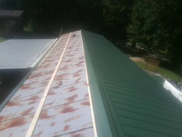 Old rusted panels beside newly installed green metal roofing — Wind Damage Roof Repair by Roofing Brothers in Brownell