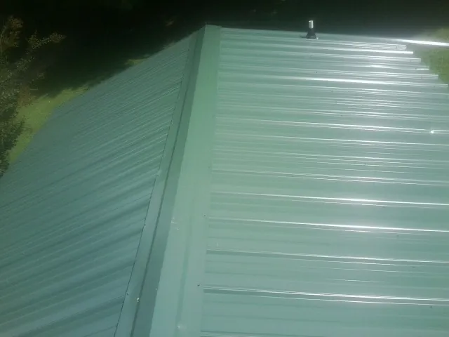New green metal panels meeting at the ridge of a roof — Flat Roof Repair work by our crew in Brownell