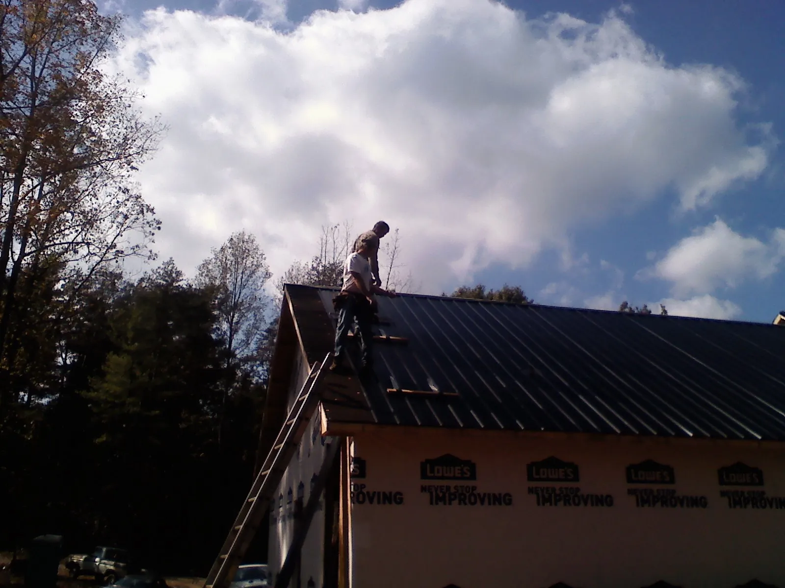 Roofer fastening dark metal panels high against a cloudy sky, from a Roof Inspection job in Brownell