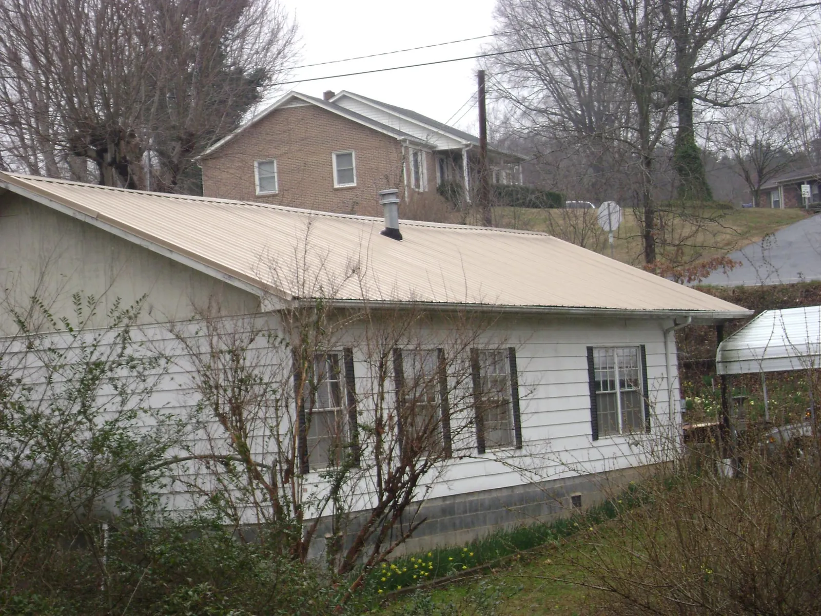 Tan metal roof on a white sided house set into a hillside in Brownell